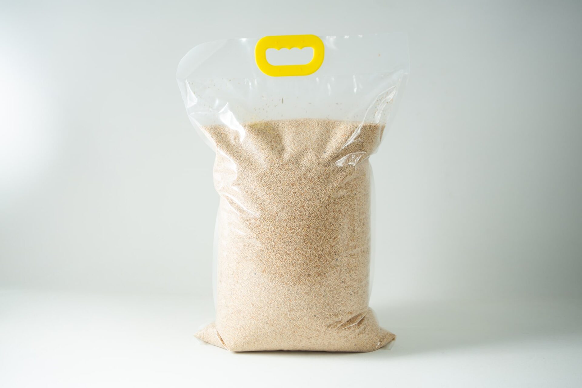 White French Millet unhulled 2 A clear plastic bag containing Certified Organic Biodynamic Rye berry grain, light brown granules, sealed with a yellow handle at the top.
