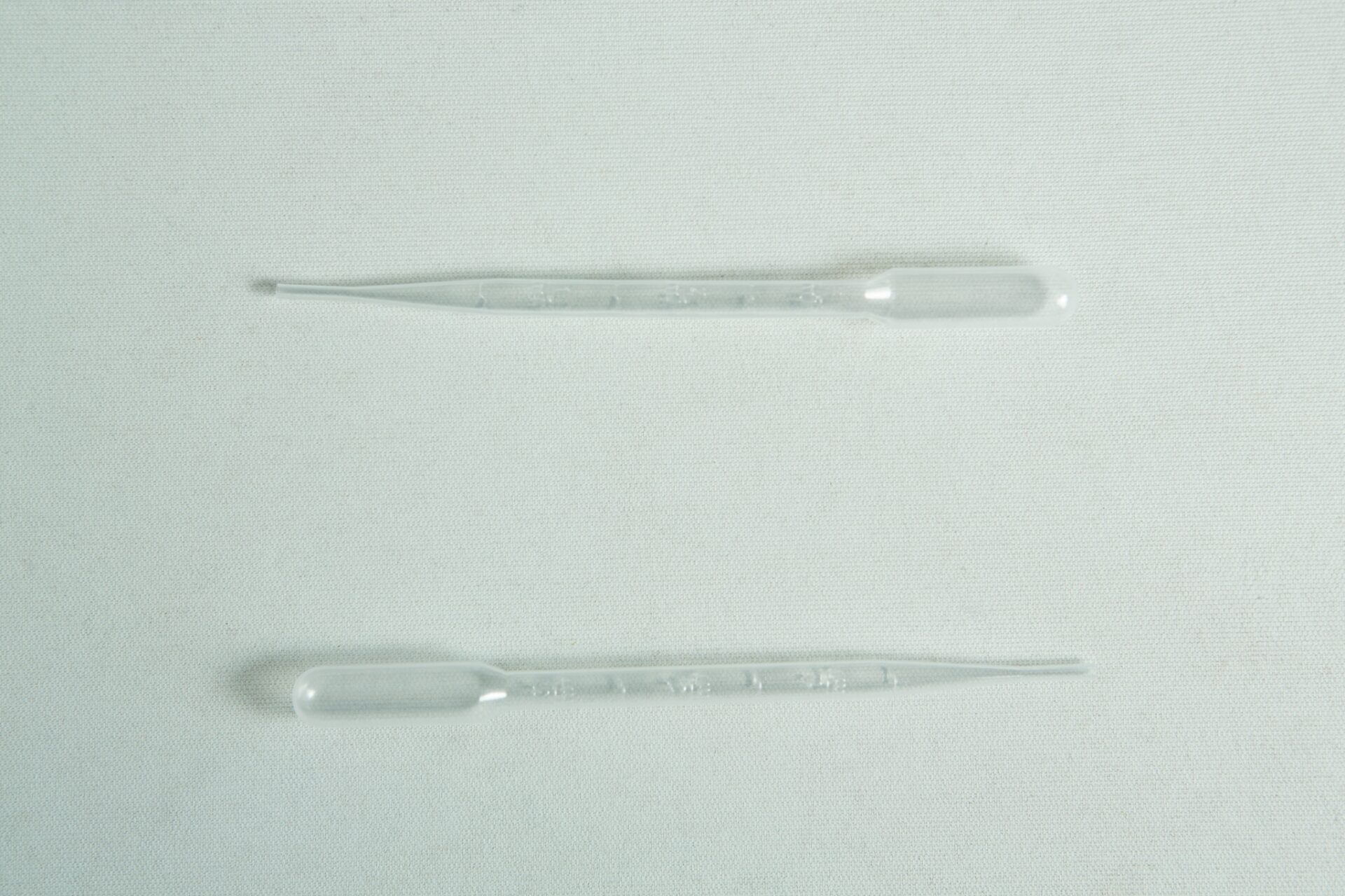 Plant Cell Synthetic Seed Starter Kit 2 Two clear plastic pipettes from the Plantcell Synthetic Seed Starter Kit lie parallel on a light, textured surface.