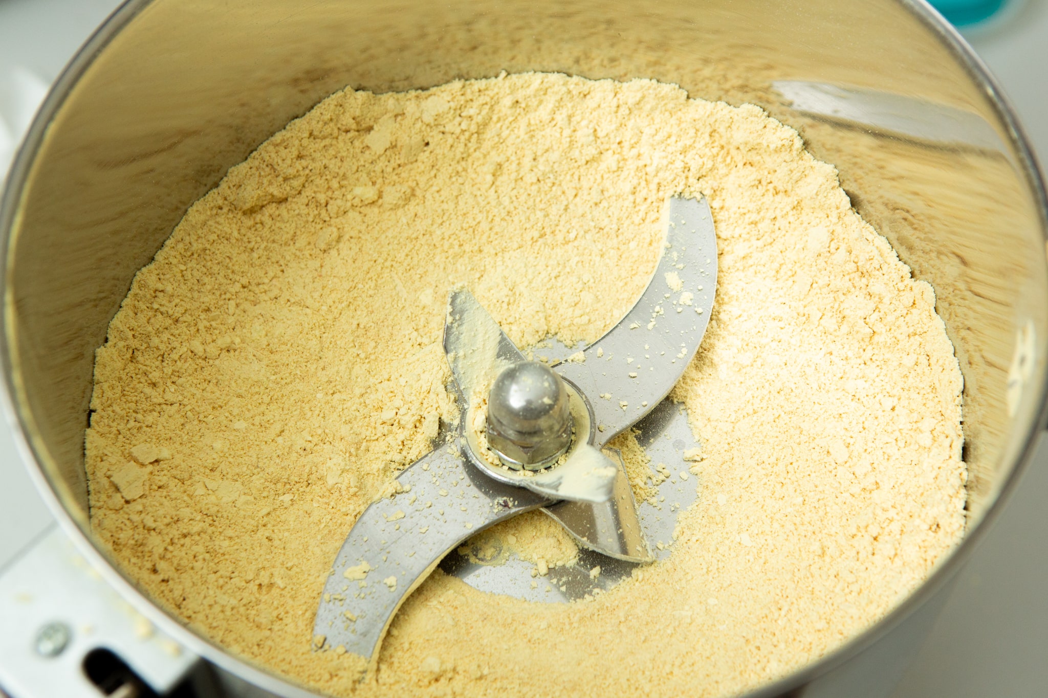 Lions Mane Mushroom Powder 100% Australian grown 100% fruiting body! 3 Close-up of Freeze-Dried Mushroom Lion’s Mane in a food processor, showing finely ground yellow powder and sharp metal blades inside.