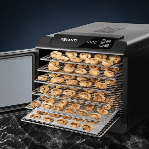 The Devanti 6 Trays Food Dehydrator with stainless steel trays is shown drying sliced mushrooms on a sleek black marble surface.
