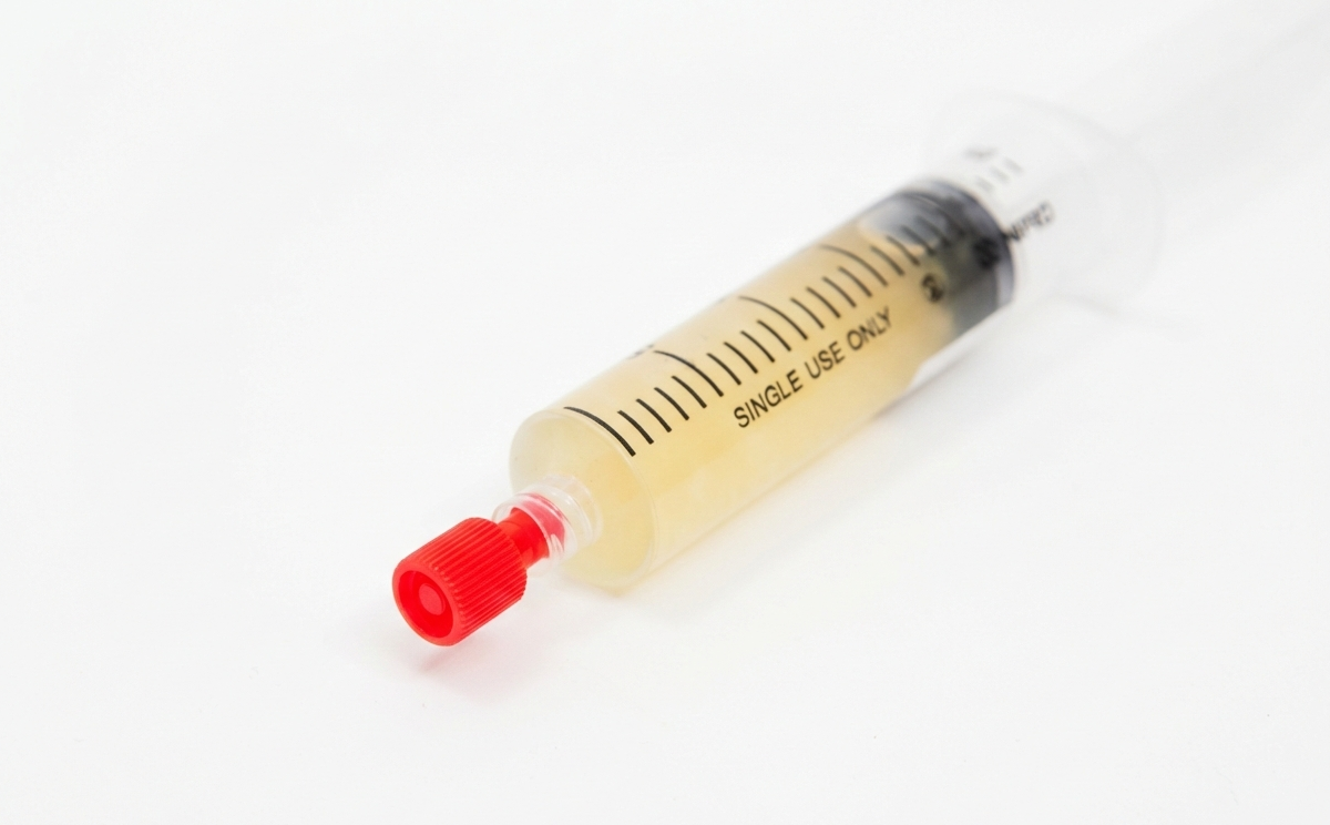 Sterile Syringe Cap for Standard Luer lock Syringe 3 A syringe filled with a yellowish liquid, capped with a red sterile syringe cap, rests on a white background.