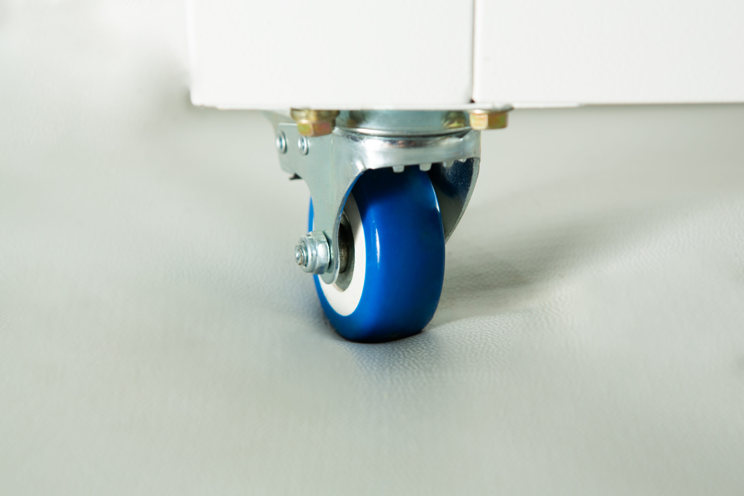 Horizontal Laminar Flowhood Cabinet | Clean bench 5 Close-up of a blue castor wheel attached to the bottom of a white piece of furniture on a light surface.