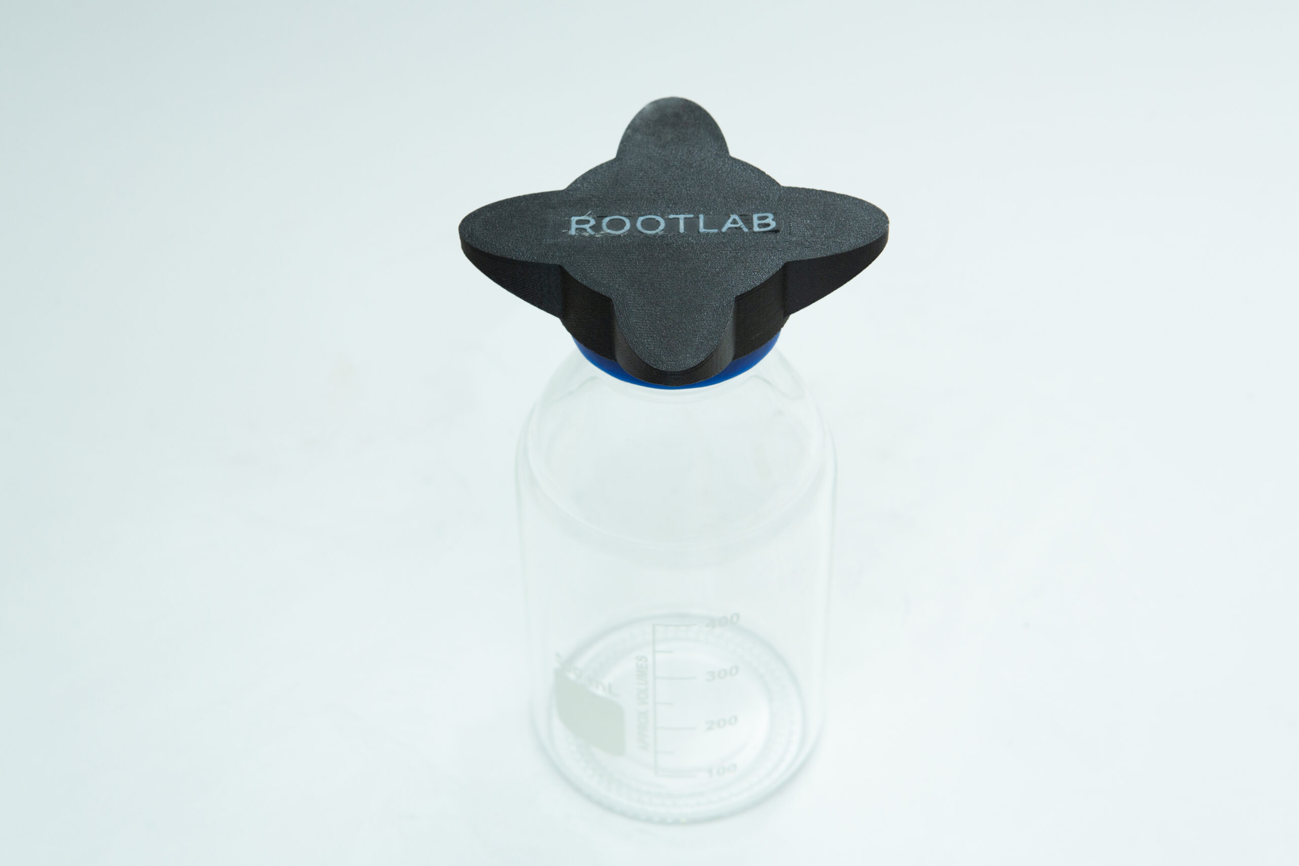 Reagent Bottle Cap Wrench | Rootlab Original | 3D Printed 6 Clear lab bottle with black, cross-shaped ROOTLAB cap, on a white background.