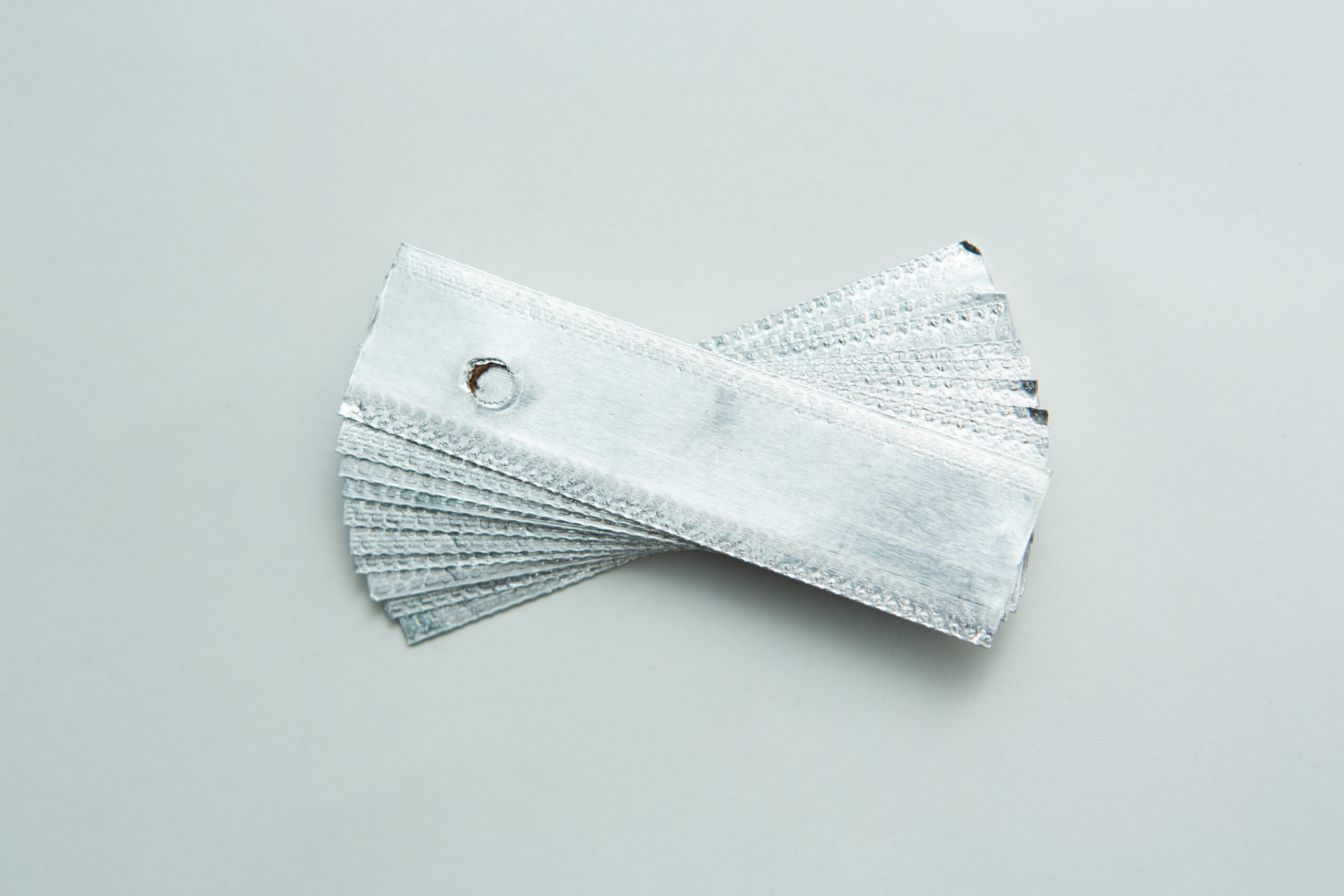 Aluminium Log Labelling Tags - Weather Safe 2 A stack of silver metal texture samples held together by a metal ring on a light grey surface.